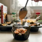 Drizzling spicy mayo over a muffin tin sushi cup with crispy nori edges